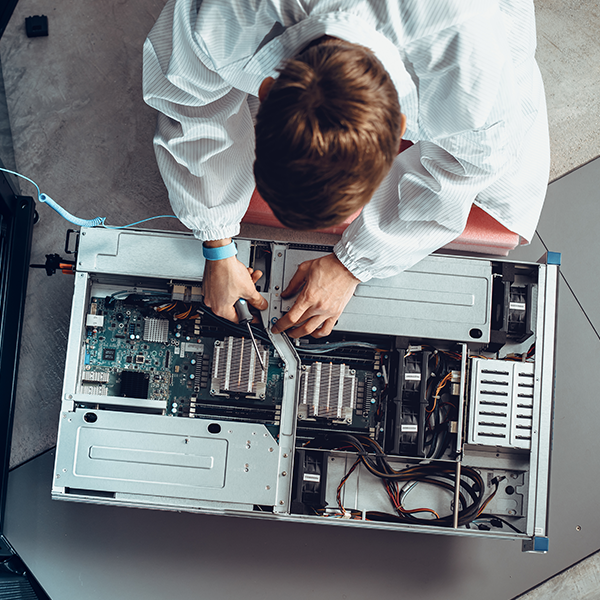 Top-down view of a person holding a screwdriver and removing hardware from a server, with exposed wiring and circuitry visible. Top-down view of a person holding a screwdriver and removing hardware from a server, with exposed wiring and circuitry visible.