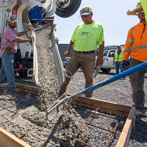 Construction workers pour concrete from a large mixing truck into a frame on the ground Construction workers pour concrete from a large mixing truck into a frame on the ground