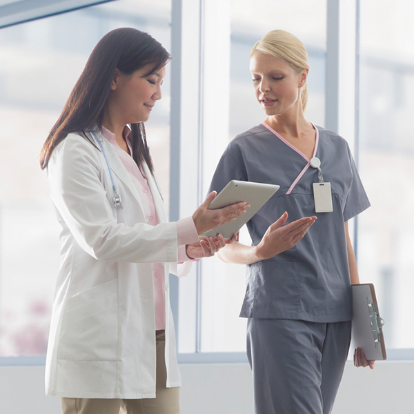 Two healthcare professionals standing and reviewing a tablet together. Two healthcare professionals standing and reviewing a tablet together.