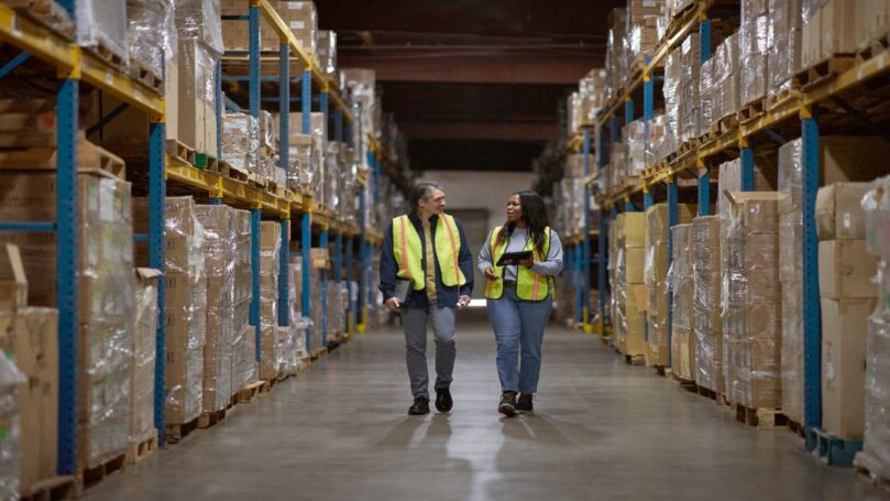 Warehouse workers walking through the aisle; manager reviewing and sharing data real time