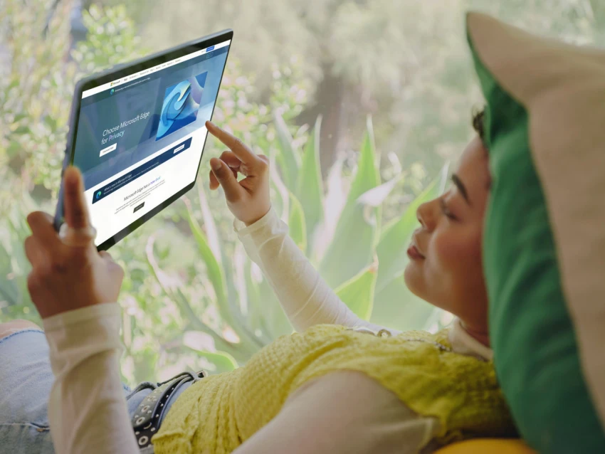 Decorative, a person laying back and holding up a tablet, using touch screen on Surface Pro 9 with Microsoft Edge on screen.