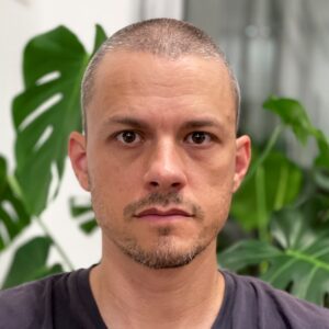 A man with a goatee and a plant behind him