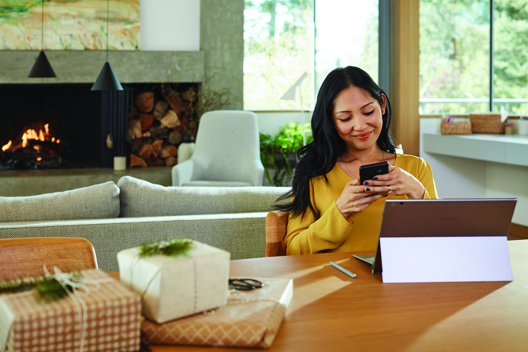 Image of a woman sitting in front of a Surface, lookin at a phone.