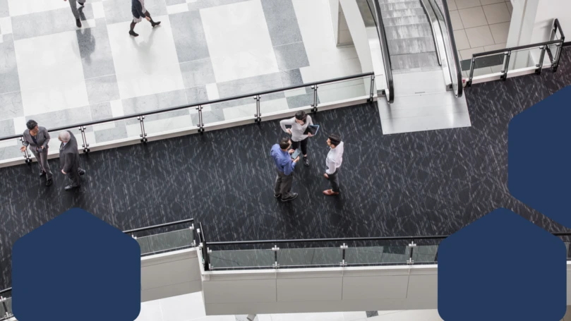 A group of people standing on a floor of a building lobby discussing
